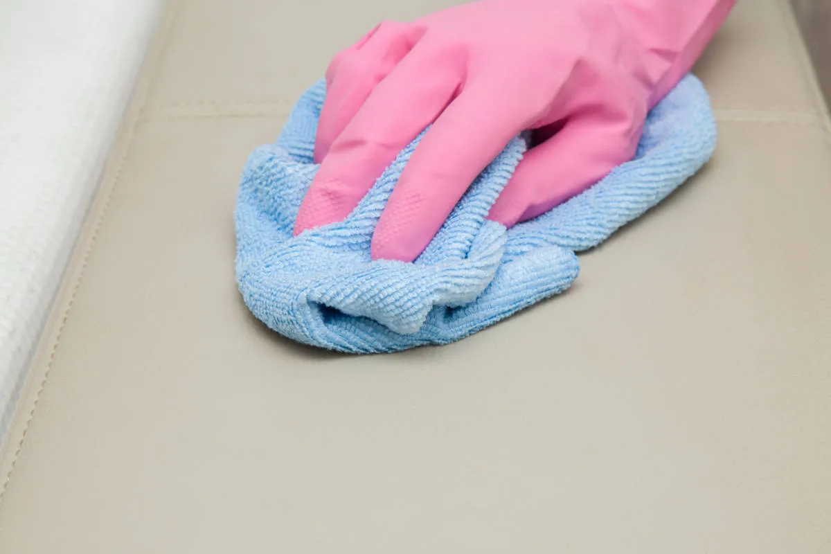 een hand met een roze handschoen die het oppervlak afveegt met een vochtige handdoek of doek' title=