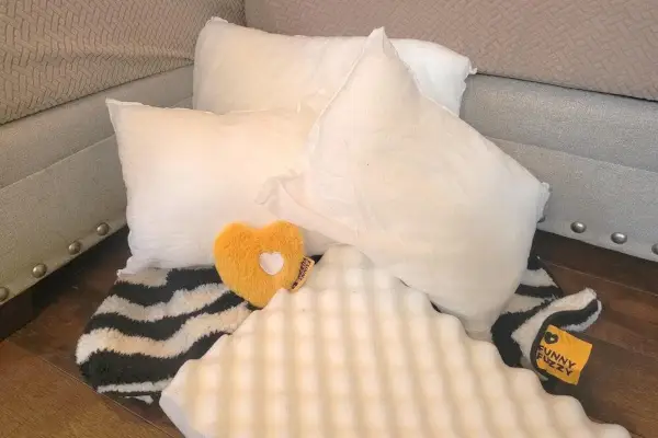 El contenido del envío de FunnyFuzzy incluye cuatro almohadas blancas, una funda a rayas blancas y negras, una almohadilla de espuma en forma de caja de huevos y un juguete de peluche con forma de corazón amarillo.