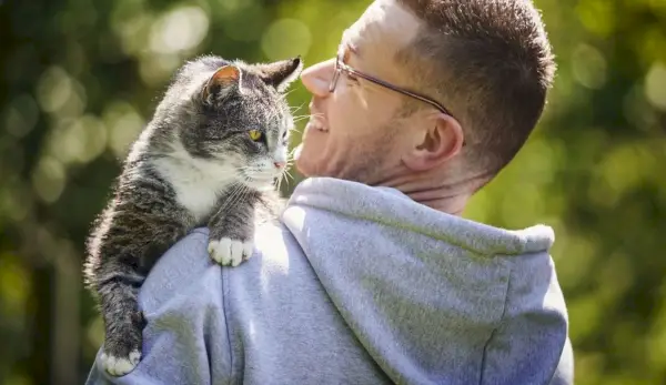 Homme souriant portant son chat tigré senior dans le jardin