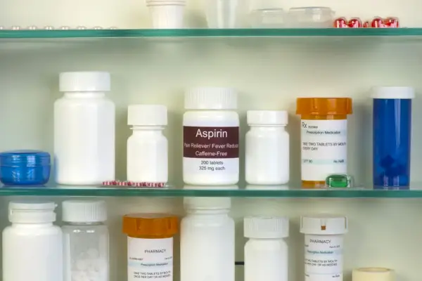 Armoire à pharmacie avec une bouteille d'aspirine, soulignant la nécessité de conserver les médicaments en toute sécurité, hors de portée des animaux de compagnie, y compris les chats, pour éviter toute ingestion accidentelle et tout dommage potentiel.