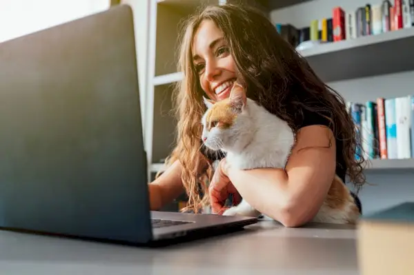 feliz joven caucásica con su gato usando una computadora portátil en casa